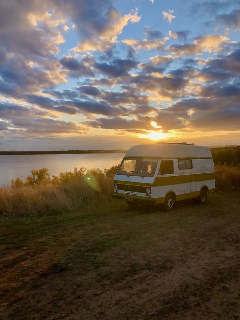 Un vieux van Volkswagen LT aménagé garé au bord d'un lac en Russie, sous un ciel de coucher de soleil